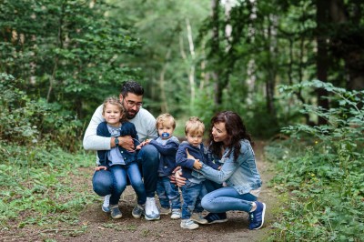 Frau und Mann mit zwei kleinen Jungs und einem Mädchen hocken auf einem Waldweg