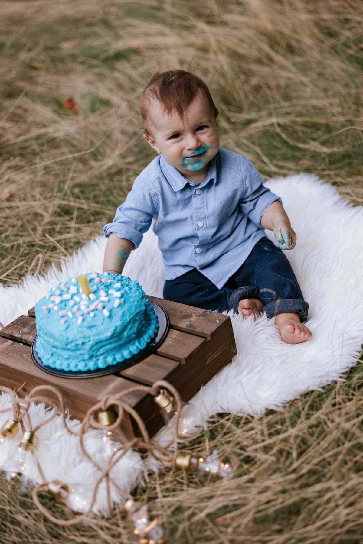 kleiner junge hat einen ganz blauverschmierten mund vom torte essen beim cakesmash fotoshoot