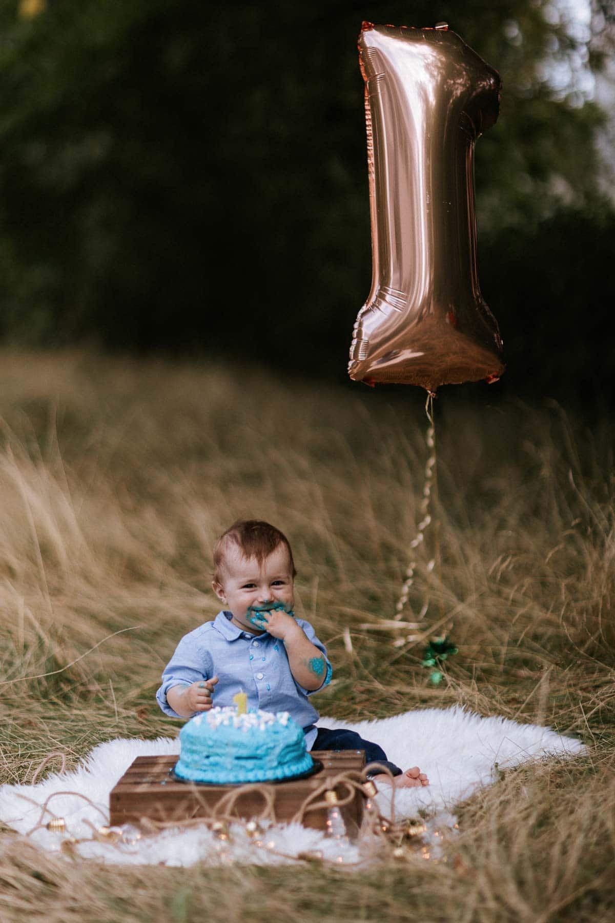 junge beim cakesmash fotoshoot sitzt vor seiner torte und im hintergrund ist ein großer ballon in form einer eins zu sehen