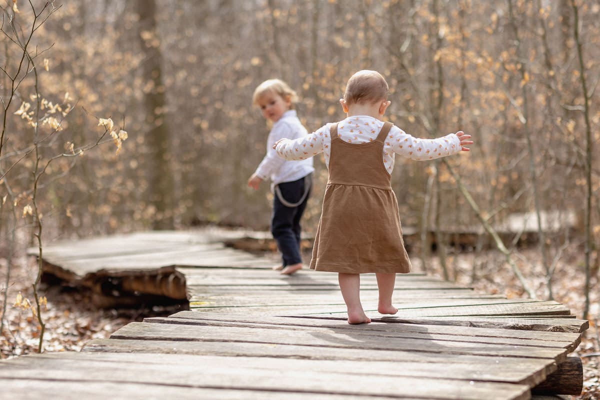 zwei kleine kinder laufen über einen brettersteg barfuß durch den wald bei meinen familienfotos im wald