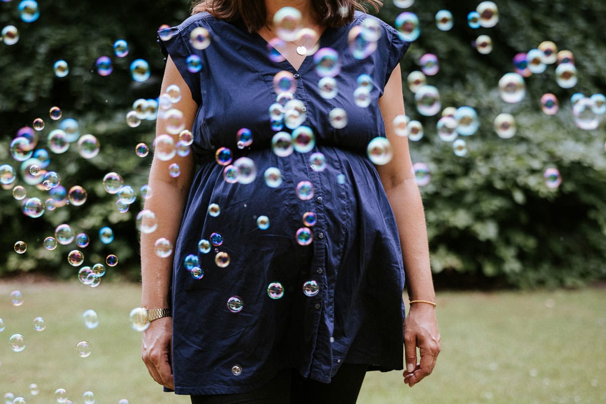 frau mit babybauch durch seifenblasen fotografiert bei einem fotoshoot im botanischen garten in braunschweig