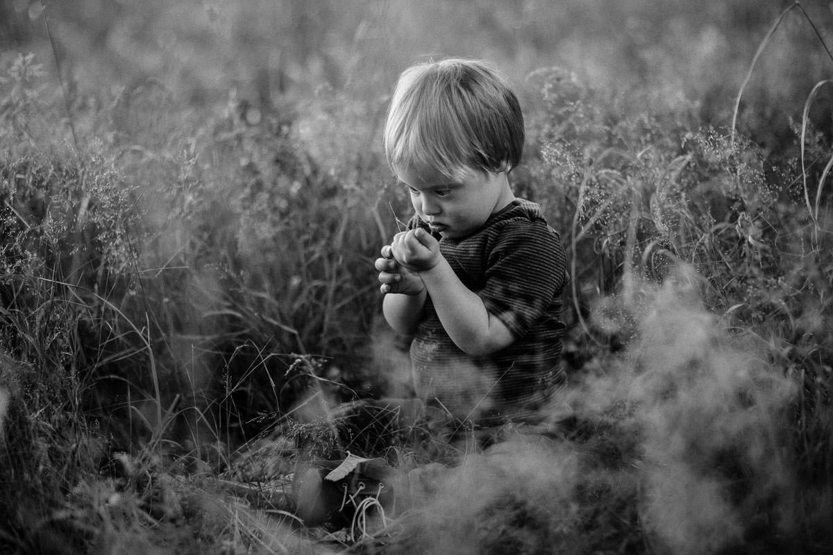 kleiner junge sitzt im hohen gras und bestaunt einzelne grashalme während der waldportraits in wolfsburg