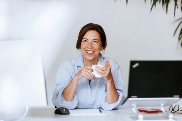 Lächelnde Frau mit einer Tasse am Schreibtisch