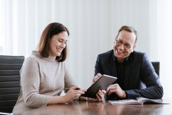 Zwei Menschen am Tisch mit Tablet, lächelnd.