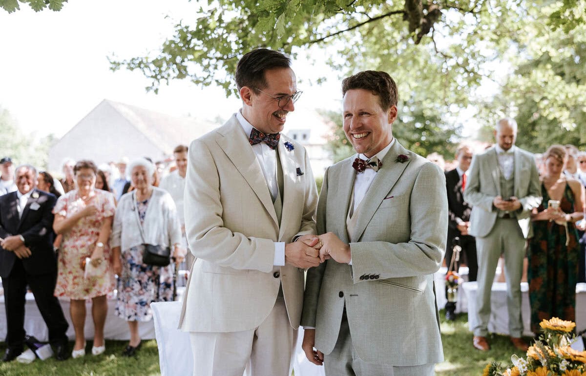 Zwei Männer heiraten im Freien vor Gästen.