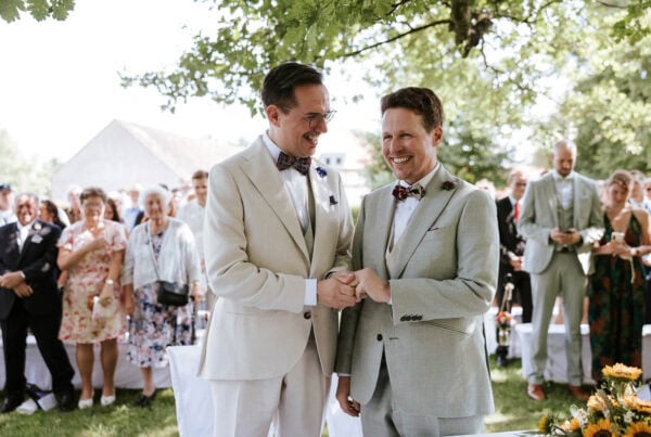 Zwei Männer heiraten im Freien vor Gästen.