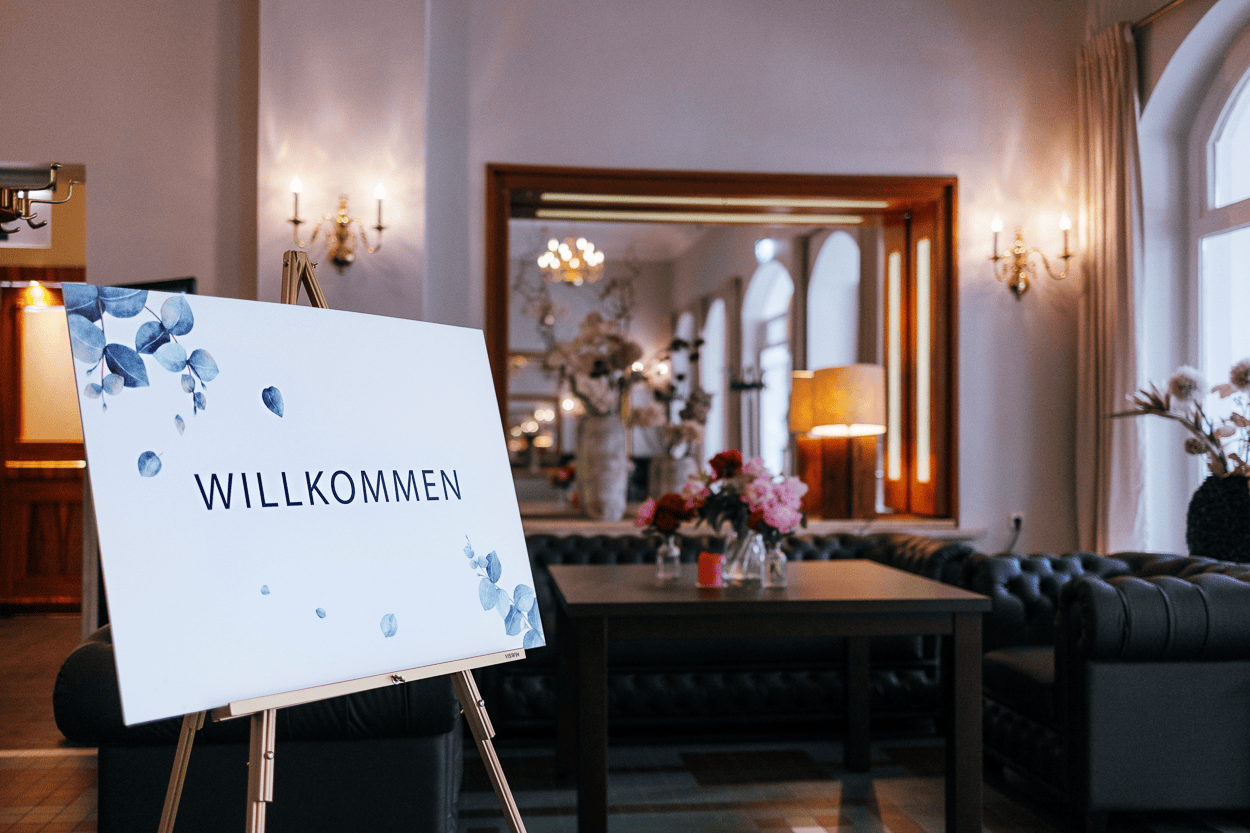 Willkommensschild in elegantem Raum mit Blumen und Spiegel.