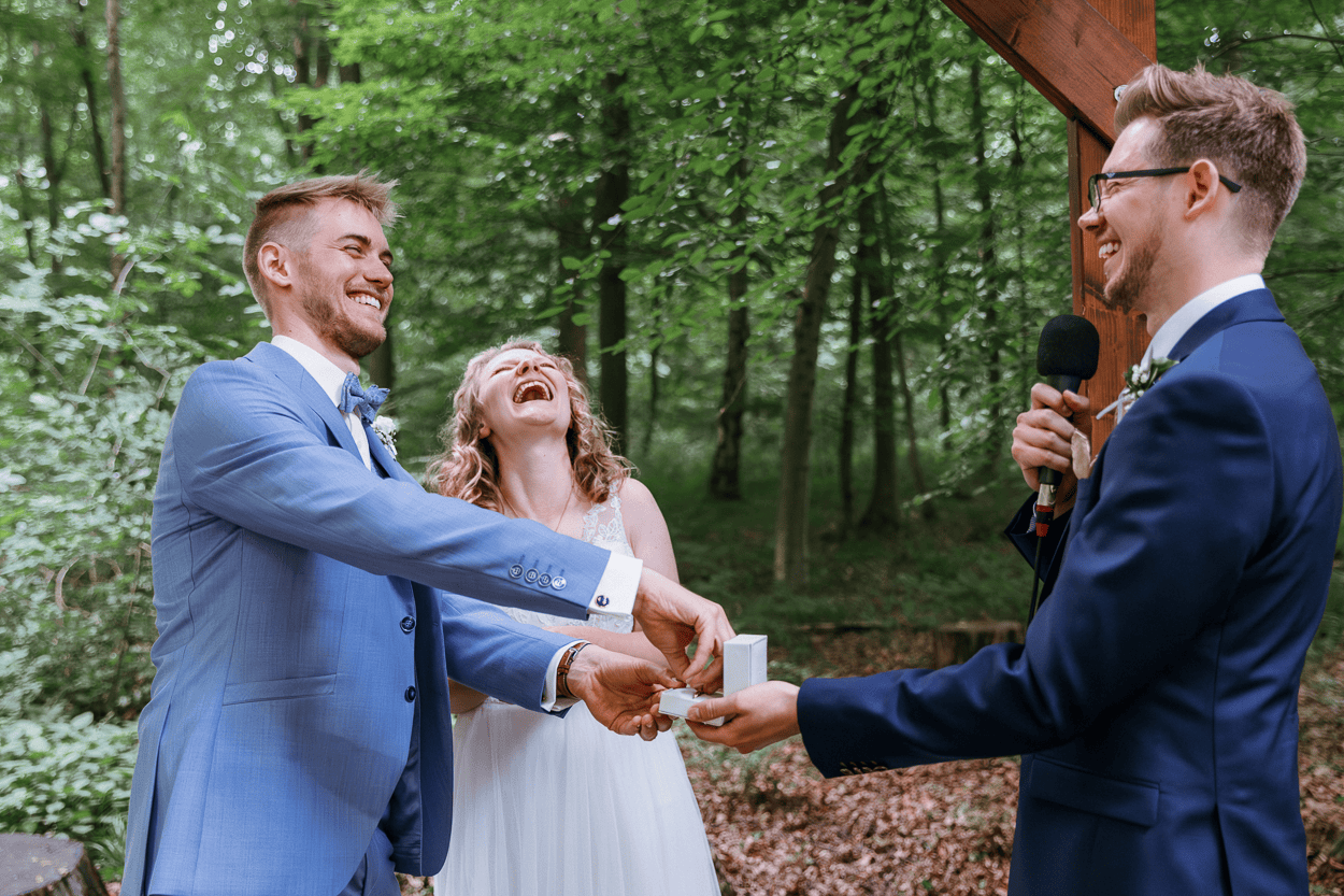 Lachendes Hochzeitspaar im Wald bei der Trauung.