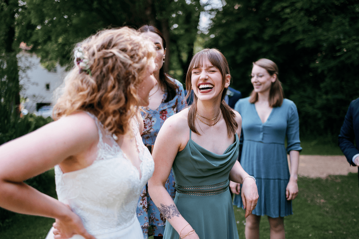 Frauen lachen zusammen auf einer Hochzeit im Freien.