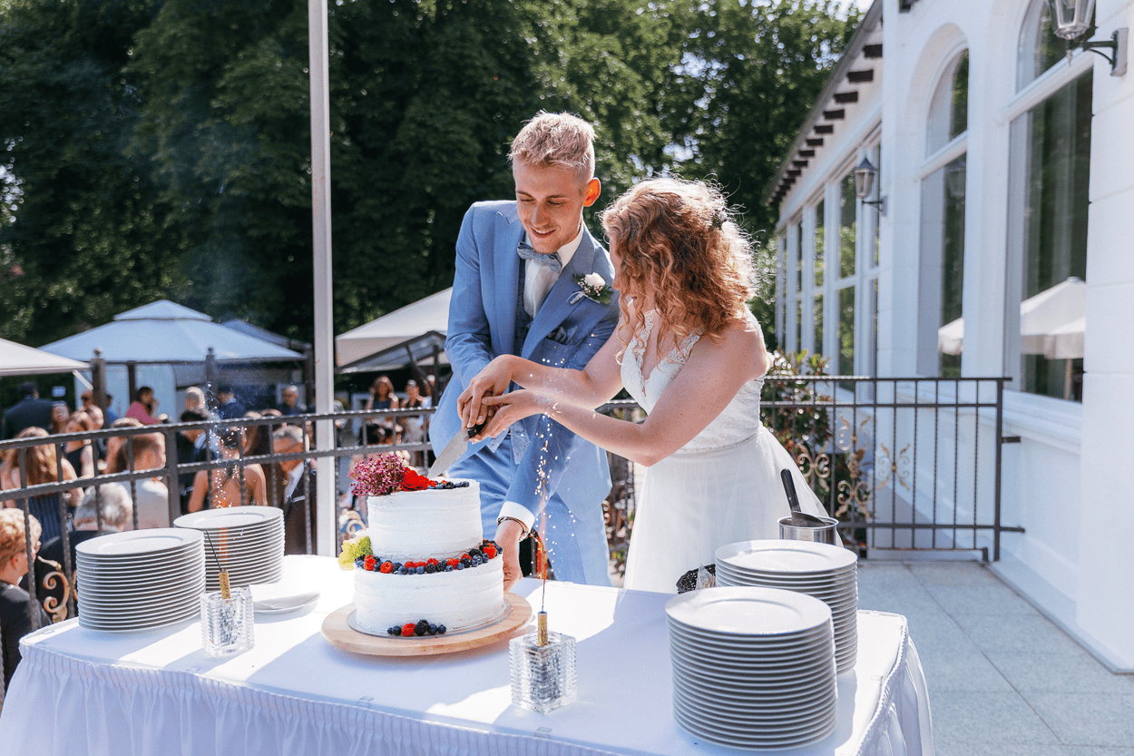 Brautpaar schneidet Hochzeitstorte an, draußen bei Feier.
