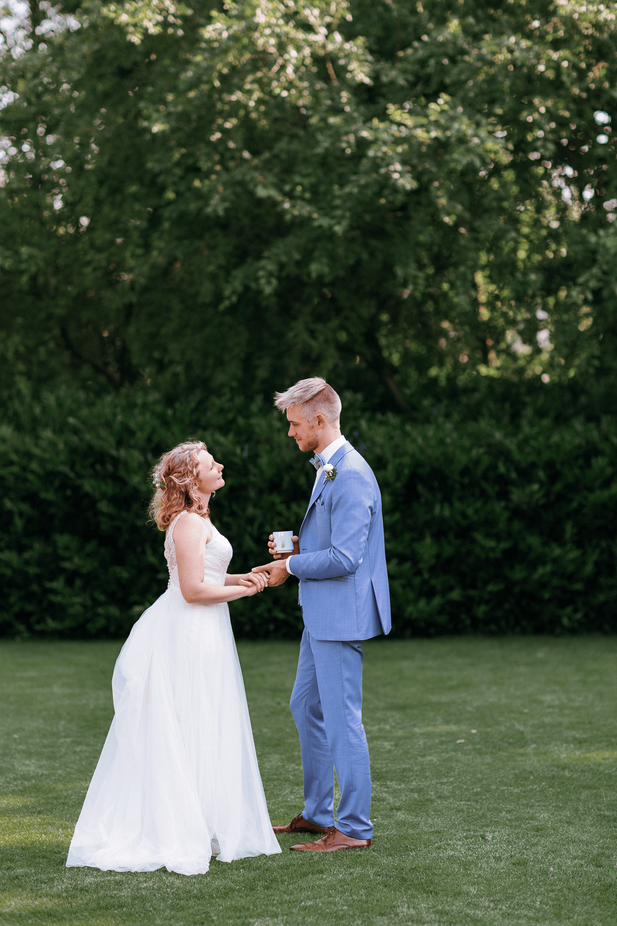 Brautpaar im Garten am Hochzeitstag hält sich an Händen und schaut sich an