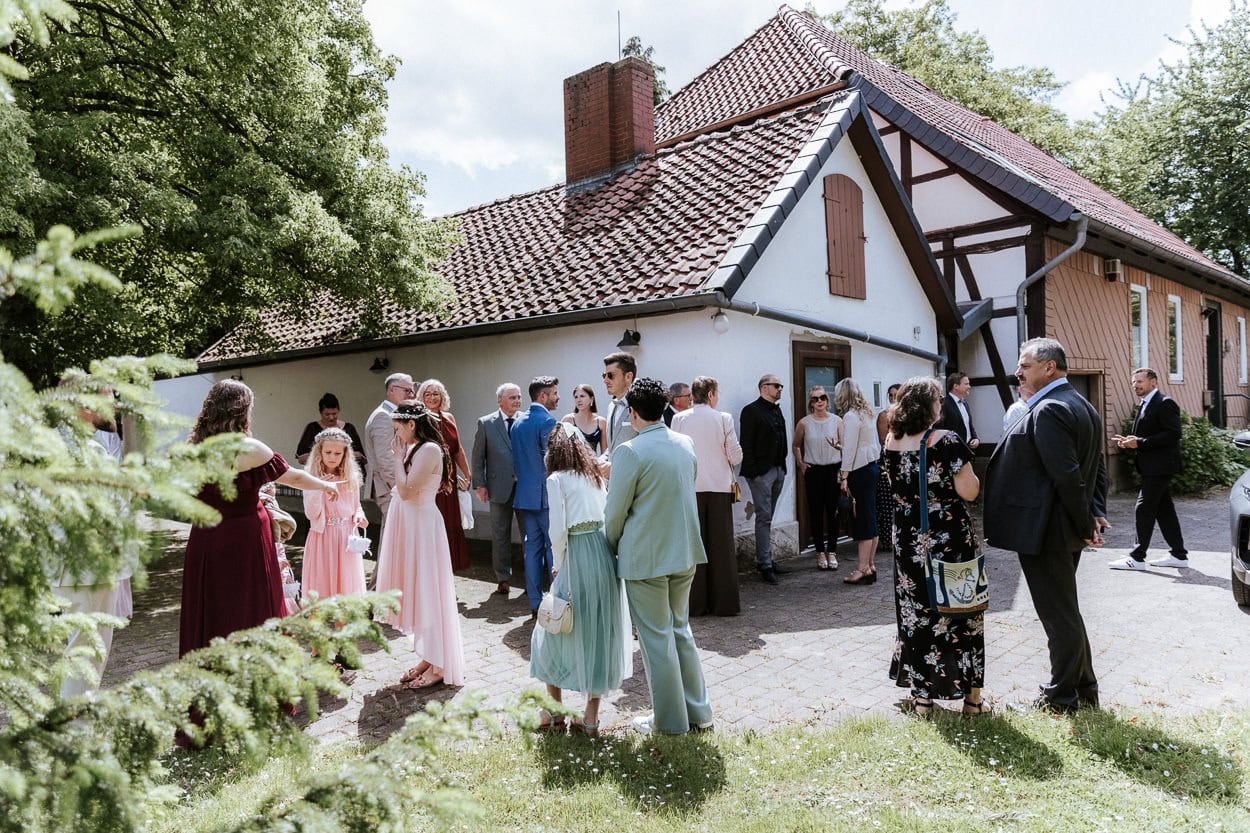 Hochzeitsgäste unterhalten sich vor einem Fachwerkhaus in der Sonne
