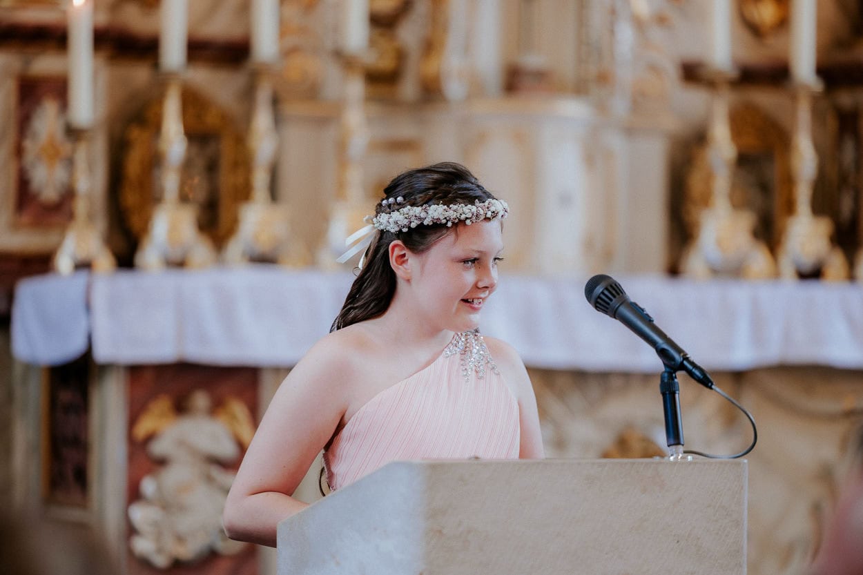 Mädchen mit Blumenkranz hält eine Rede am Rednerpult vor dem Altar