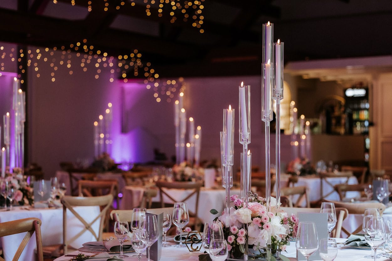 Festsaal mit gedeckten Tischen, Kerzenständern und Blumengestecken unter Lichterketten