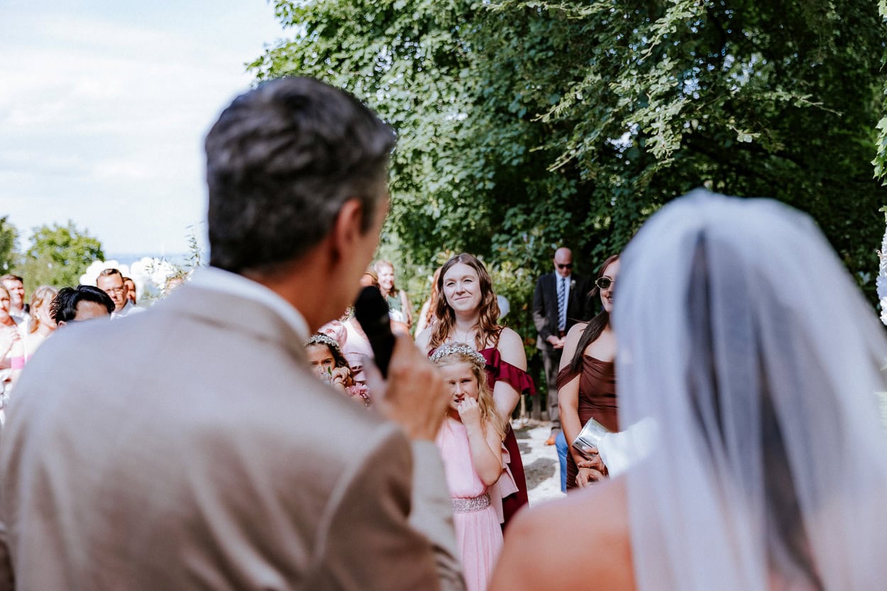 Hochzeitsgäste hören lächelnd einer Rede des Hochzeitspaares zu