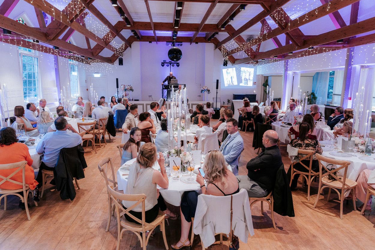Festsaal mit Hochzeitsgesellschaft an gedeckten Tischen, DJ und Diskokugel im Hintergrund