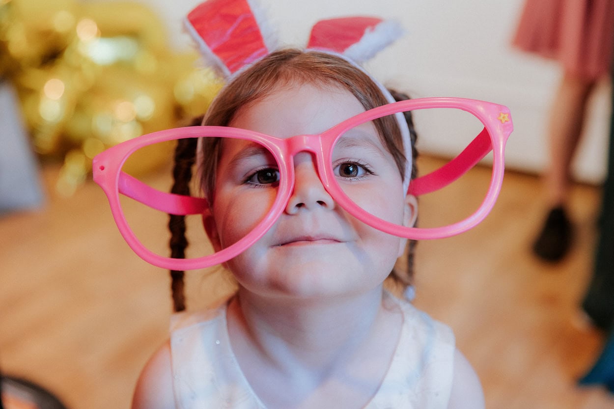 Kleines Mädchen mit übergroßer pinker Brille und Hasenohren blickt in die Kamera