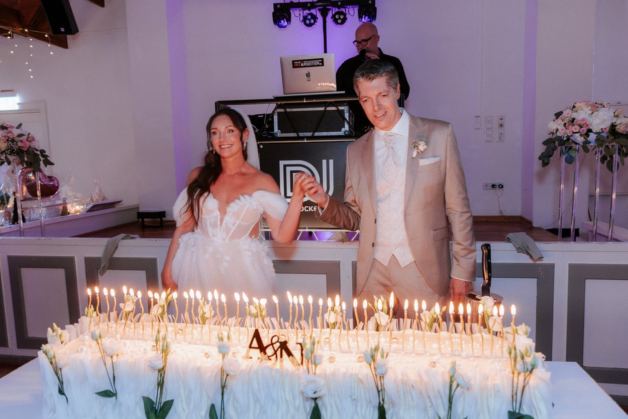 Braut und Bräutigam halten Händchen vor ihrer brennenden Hochzeitstorte mit Kerzen