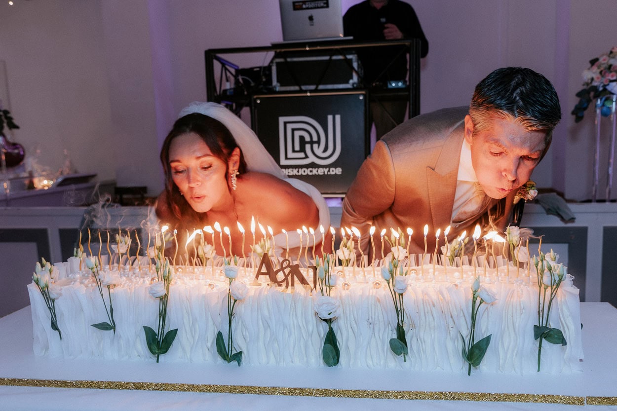 Braut und Bräutigam pusten gemeinsam die Kerzen auf der Hochzeitstorte aus