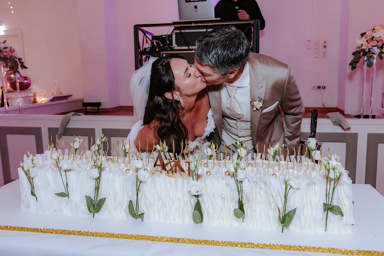 Braut und Bräutigam küssen sich hinter ihrer festlich dekorierten Hochzeitstorte